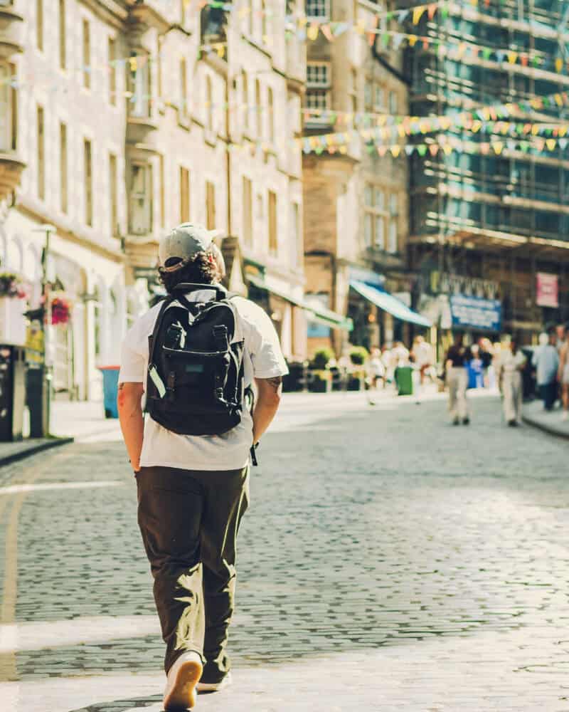 Person walking in a city street with backpack, historic buildings in the background.