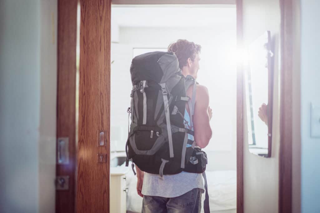Young man with backpack entering Mitte Hostel in Berlin, bright natural light.