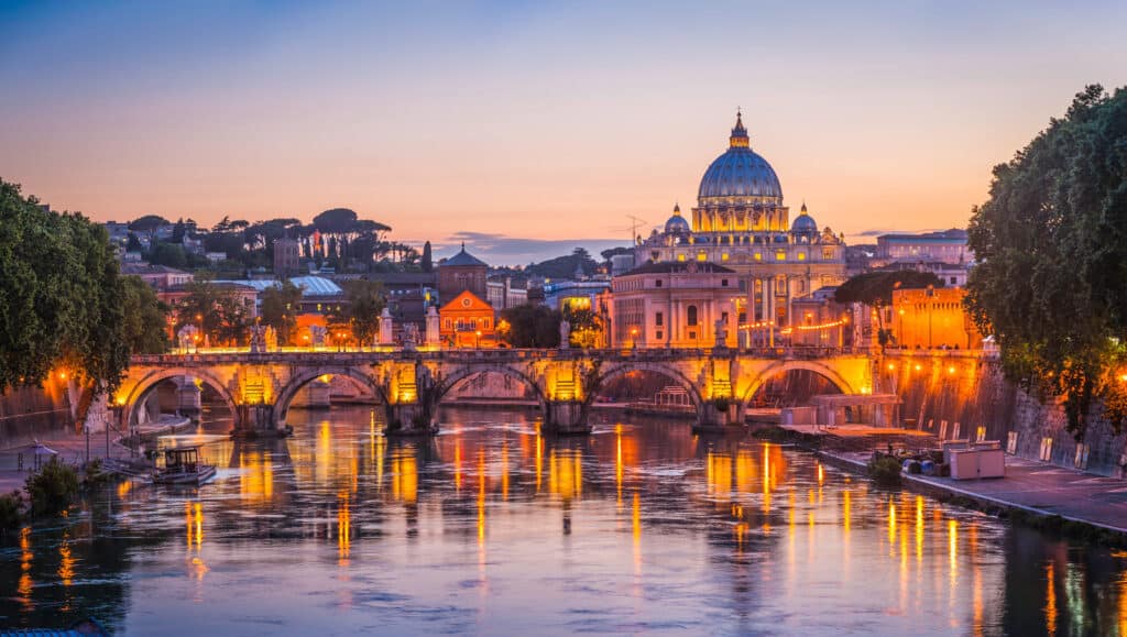 View of St. Peter's Basilica and the Tiber River in Rome at sunset, showcasing historic architecture.