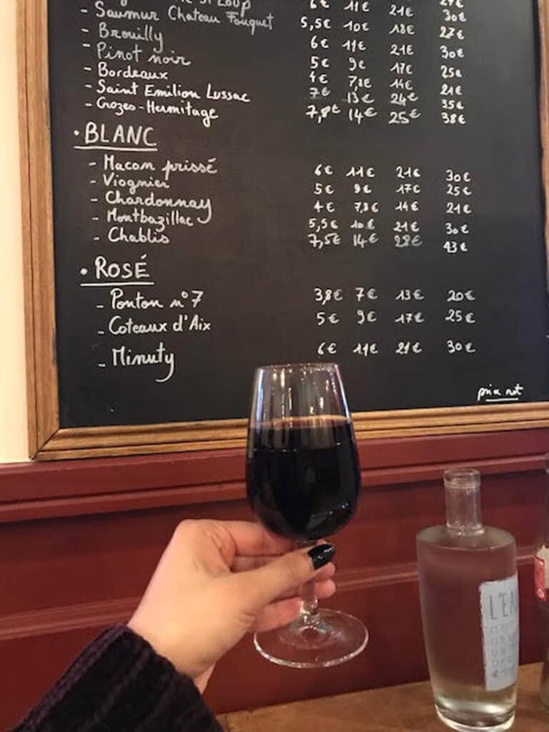 Interior of Mitte Hostel with a hand holding a glass of red wine in front of a menu board.