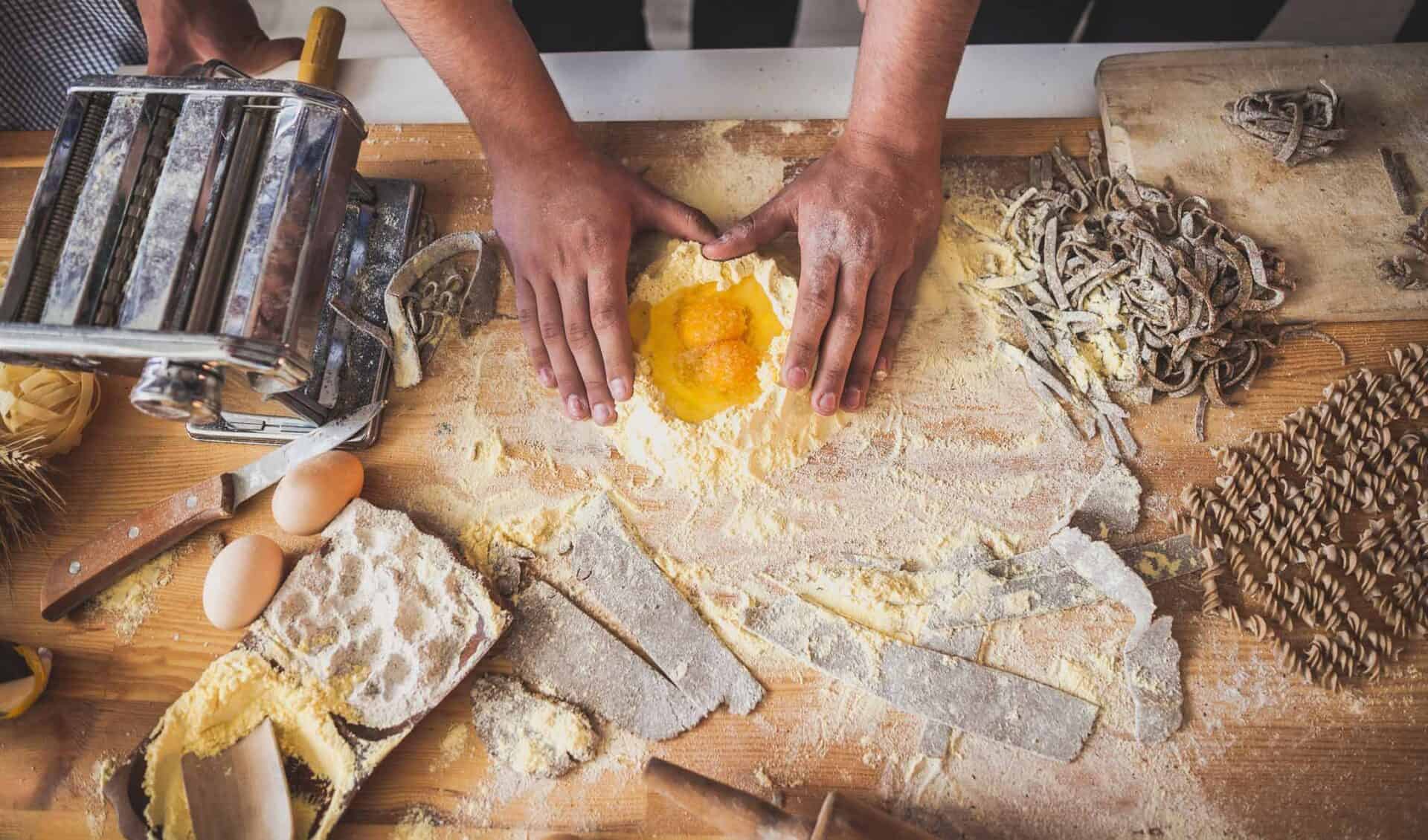 Homemade pasta being prepared with eggs, flour, and rolling pin on a rustic kitchen table.