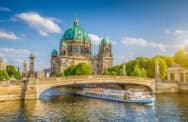 Cityscape with historic domed building and river cruise boat in the water.