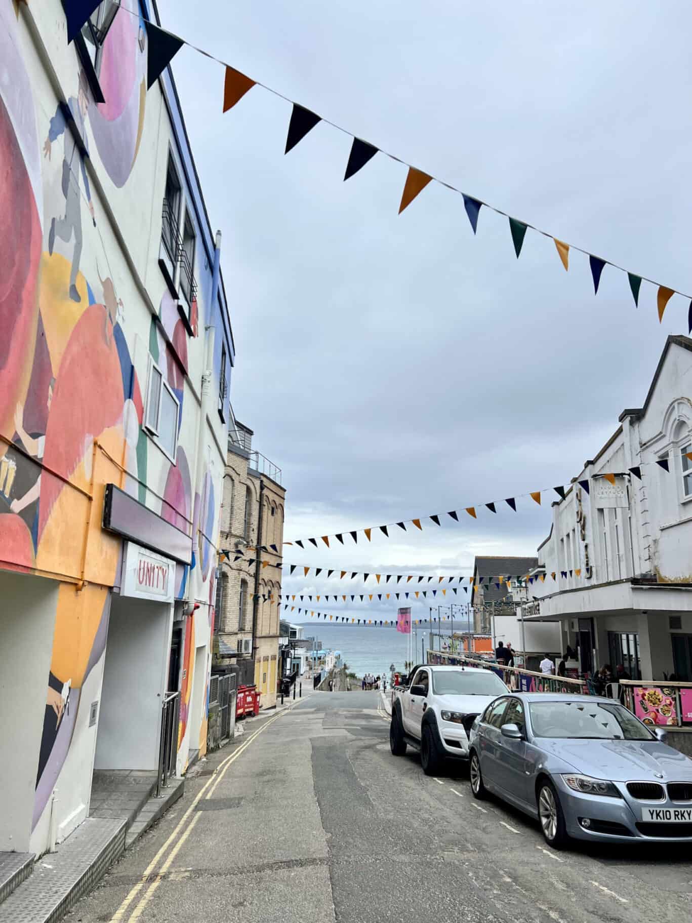 A street scene with colourful bunting and parked cars outside a hostel or bar.