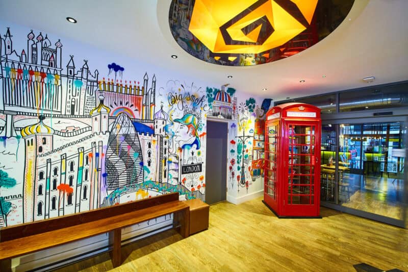 Colourful communal area with graffiti wall and red telephone box in a hostel.