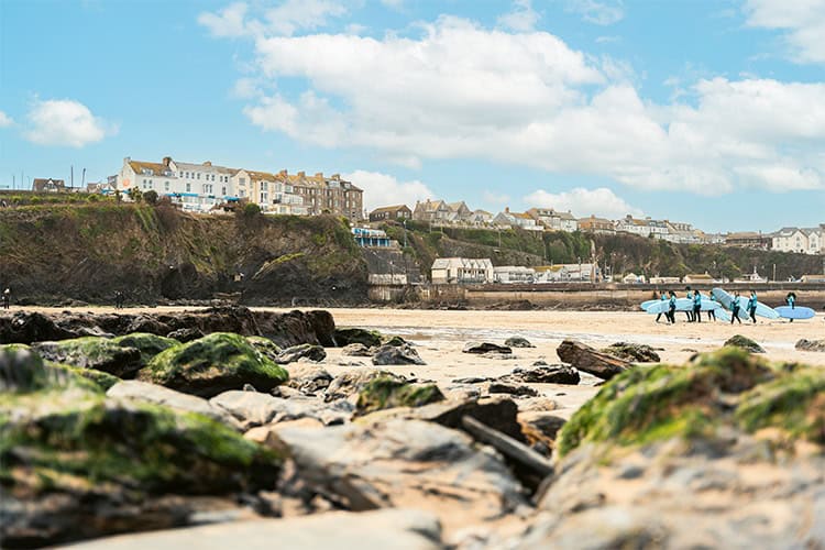 A beach scene with rocks in the foreground and a group of people with surfboards in the background.