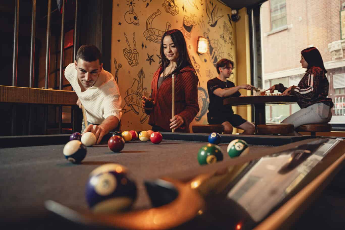 A social hostel bar with pool table and groups of travellers enjoying drinks.