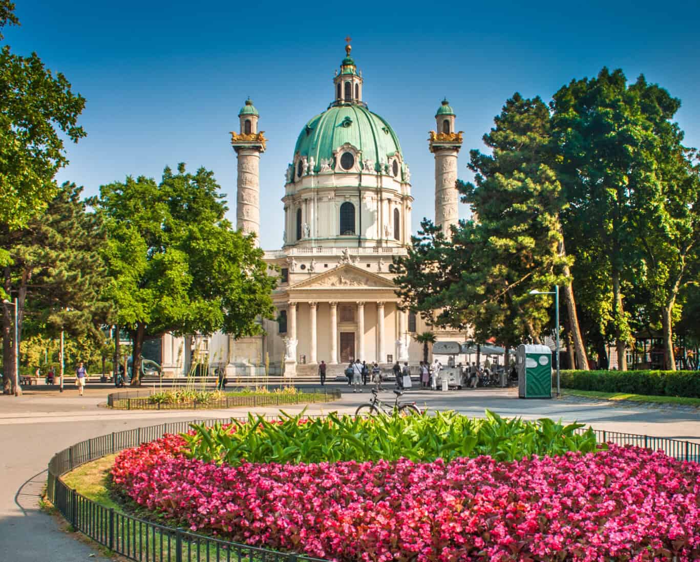 A historic church with a large green dome and four towers, surrounded by trees and a park.