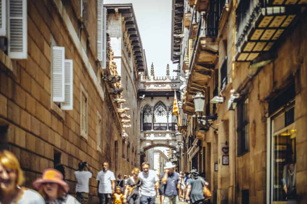 A narrow city street with historic architecture and an archway at the end, bustling with pedestrians.