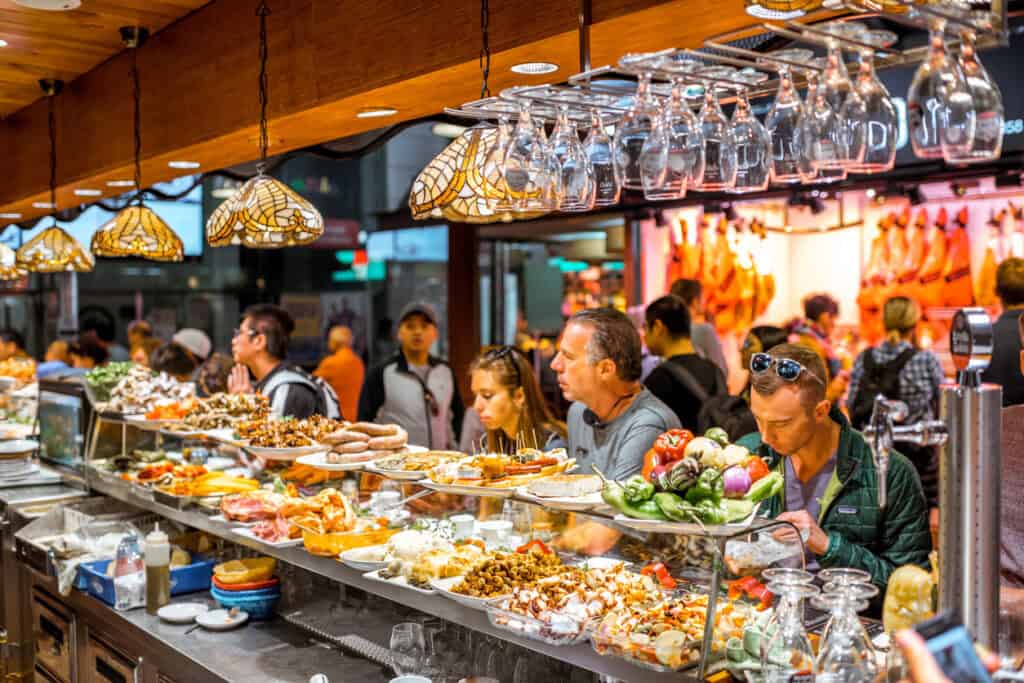 A busy social hostel bar with guests enjoying food and drinks at the counter.