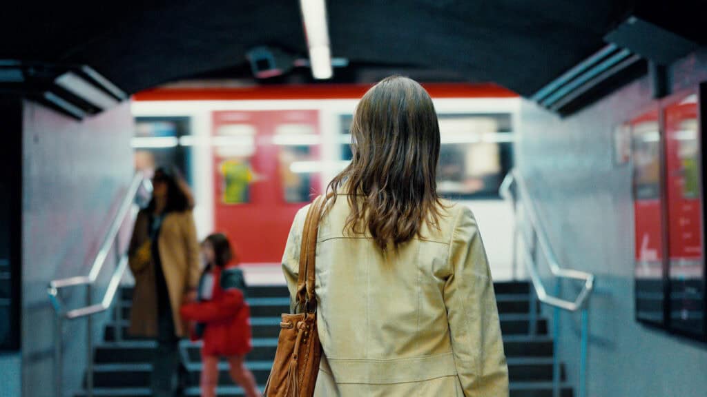 A traveller waiting at a busy underground station entrance with a train arriving.