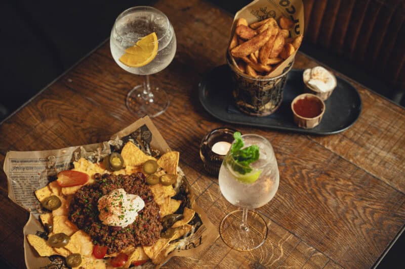 A lively social hostel bar with drinks and snacks on a wooden table.