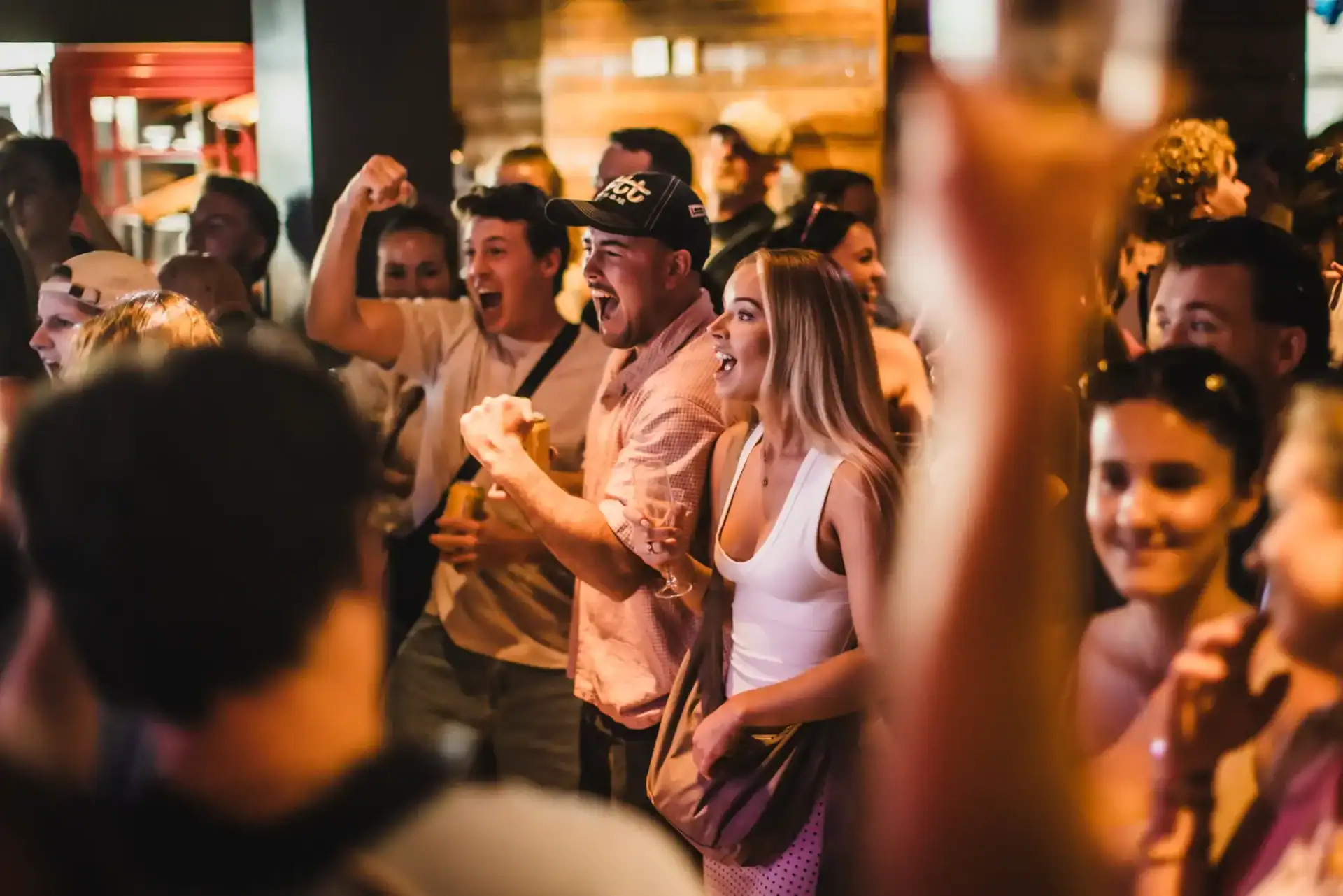 A lively social hostel bar with people enjoying drinks and entertainment.