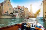 A boat on a canal with historic buildings and a tower in the background.