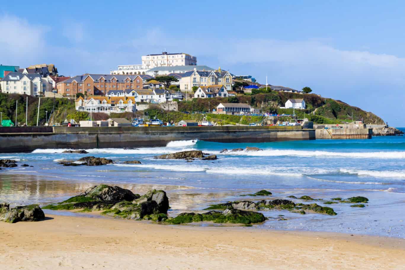 A scenic coastal view from a beach with rocks and waves, overlooking a hillside with buildings.