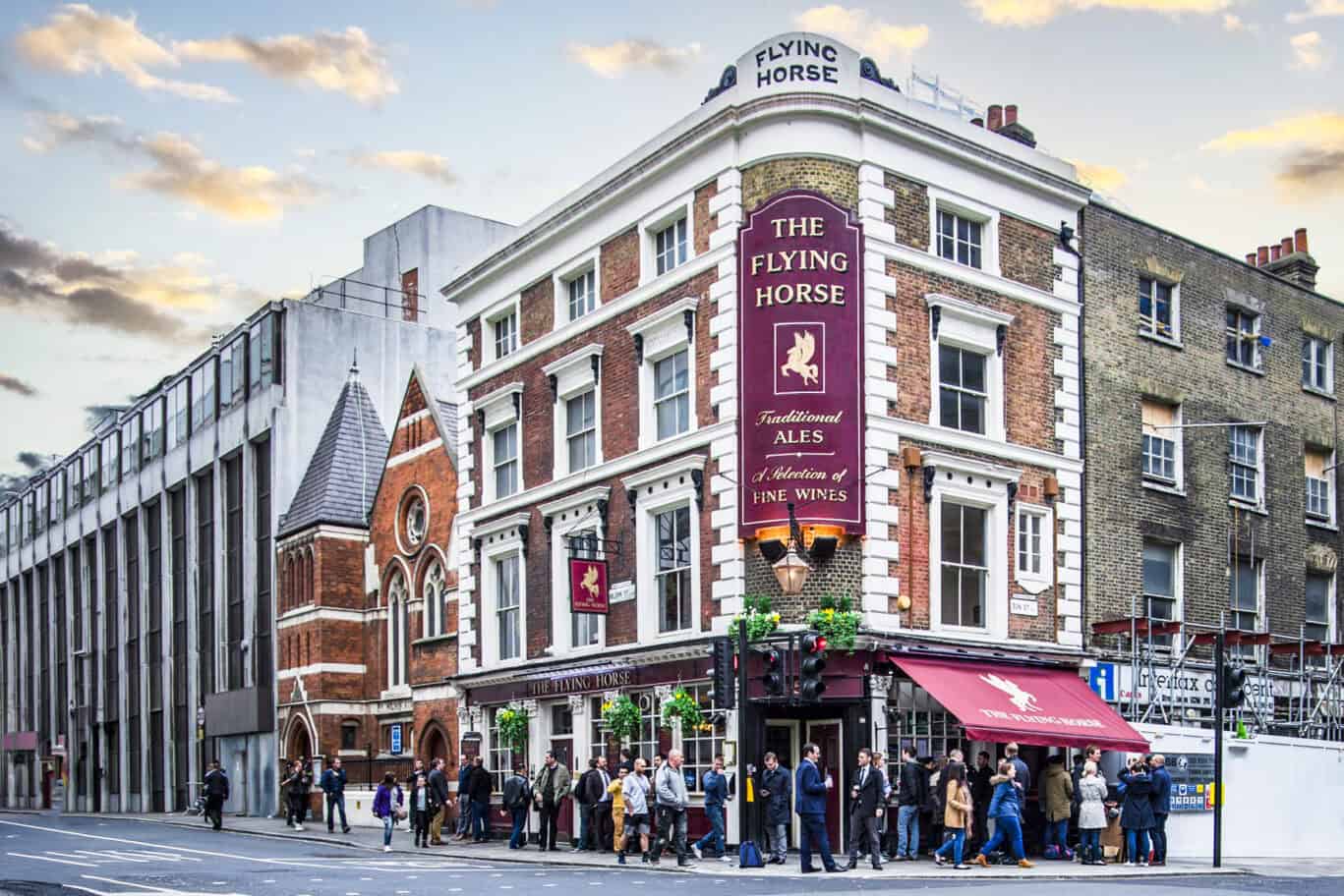 A busy social hostel bar with people gathered outside and a prominent pub sign.