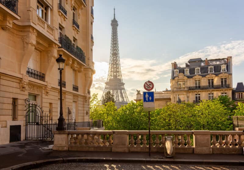 View of the Eiffel Tower from a street in Paris with classic Parisian buildings.
