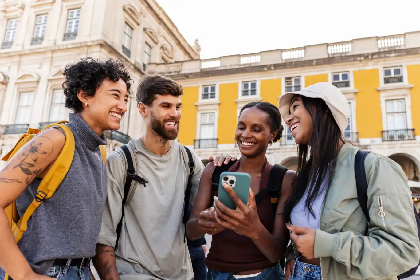 A group of young travellers smiling and looking at a phone outside a hostel.