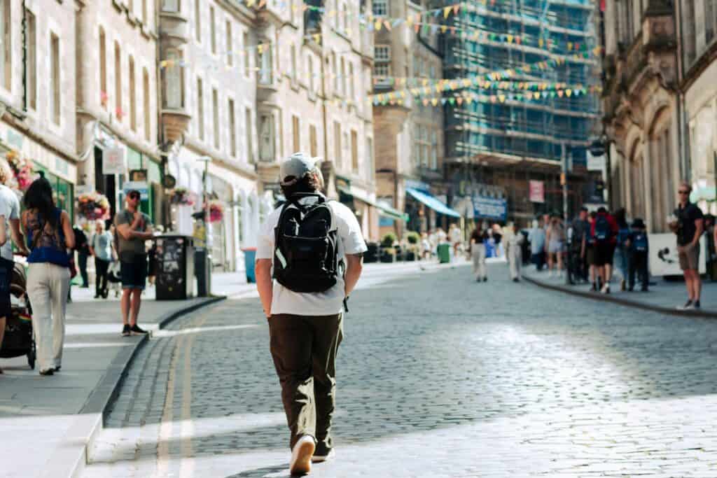 A person with a backpack walking on a busy city street in Edinburgh.