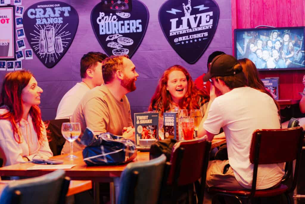 A lively social hostel bar with a group of young people enjoying drinks and conversation.