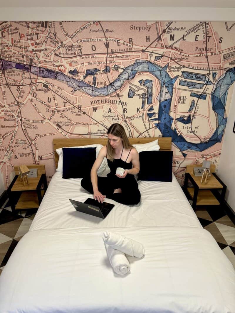 A woman working on a laptop on a queen bed in a hotel room with a city map mural.