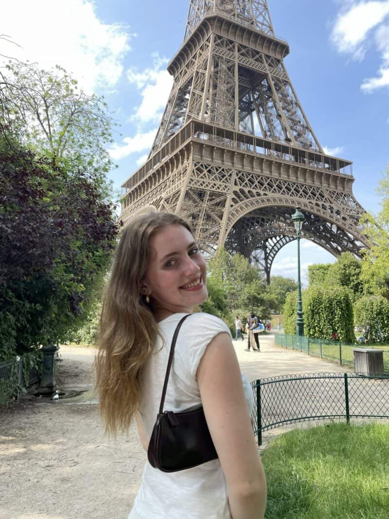 A woman visiting the Eiffel Tower in a park setting, smiling at the camera.
