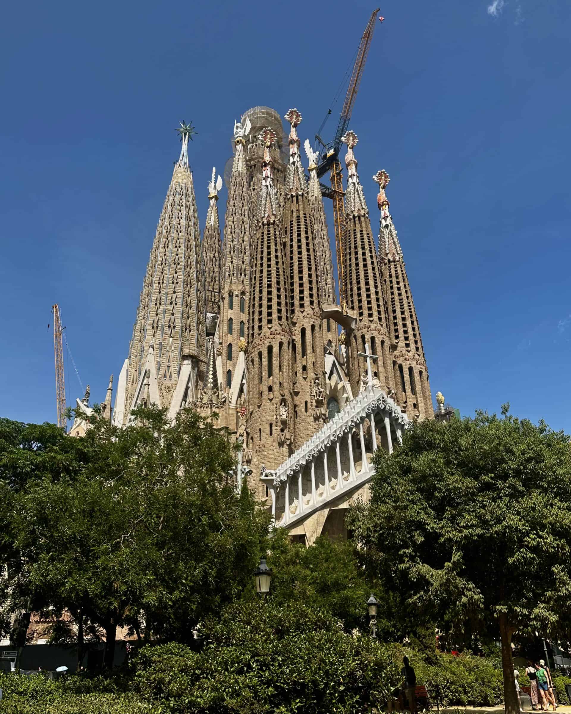 Exterior view of the Sagrada Familia with cranes and blue sky.