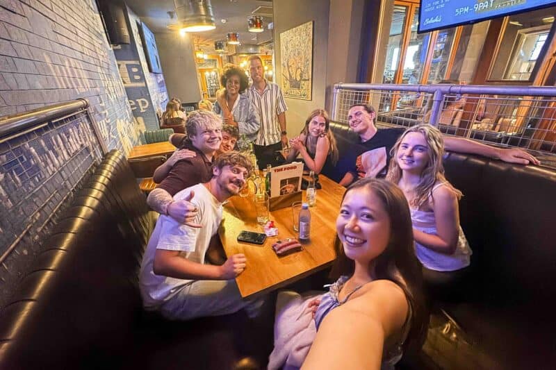 A lively social space in a hostel bar with young people enjoying drinks and conversation.