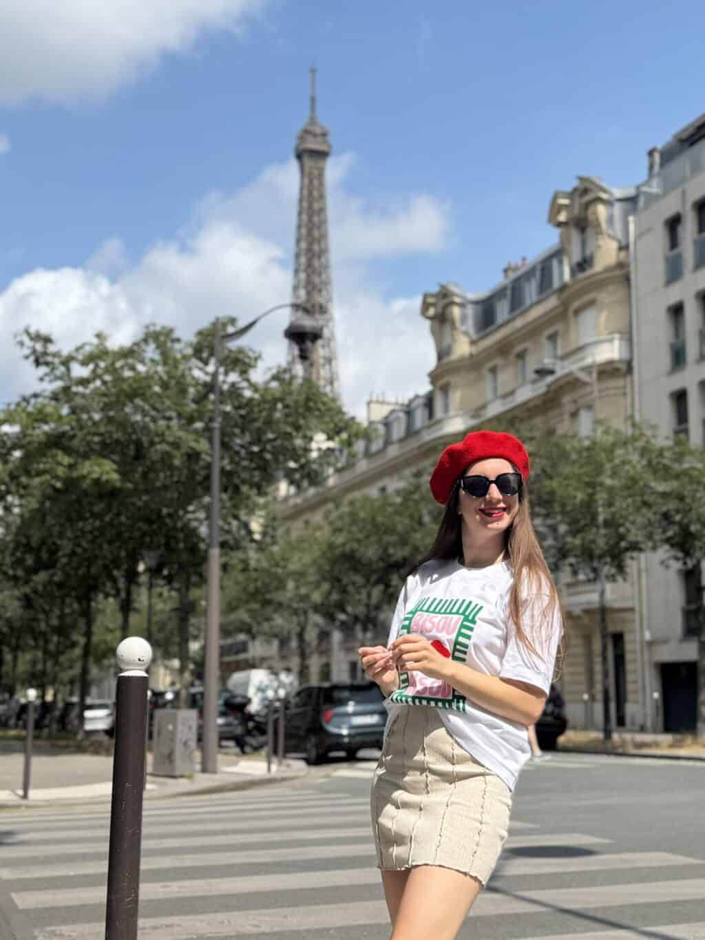 A woman in a red beret and sunglasses standing outdoors with the Eiffel Tower in the background.