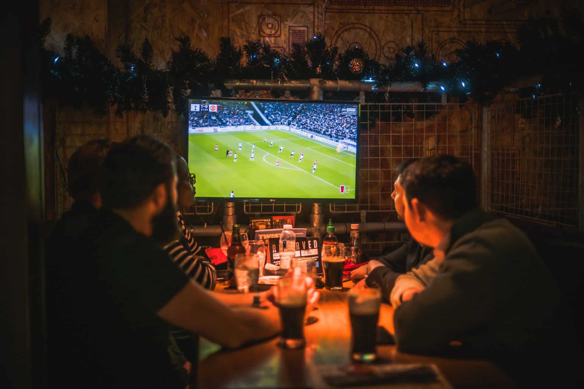 A group of friends watching a football match in a social hostel bar.