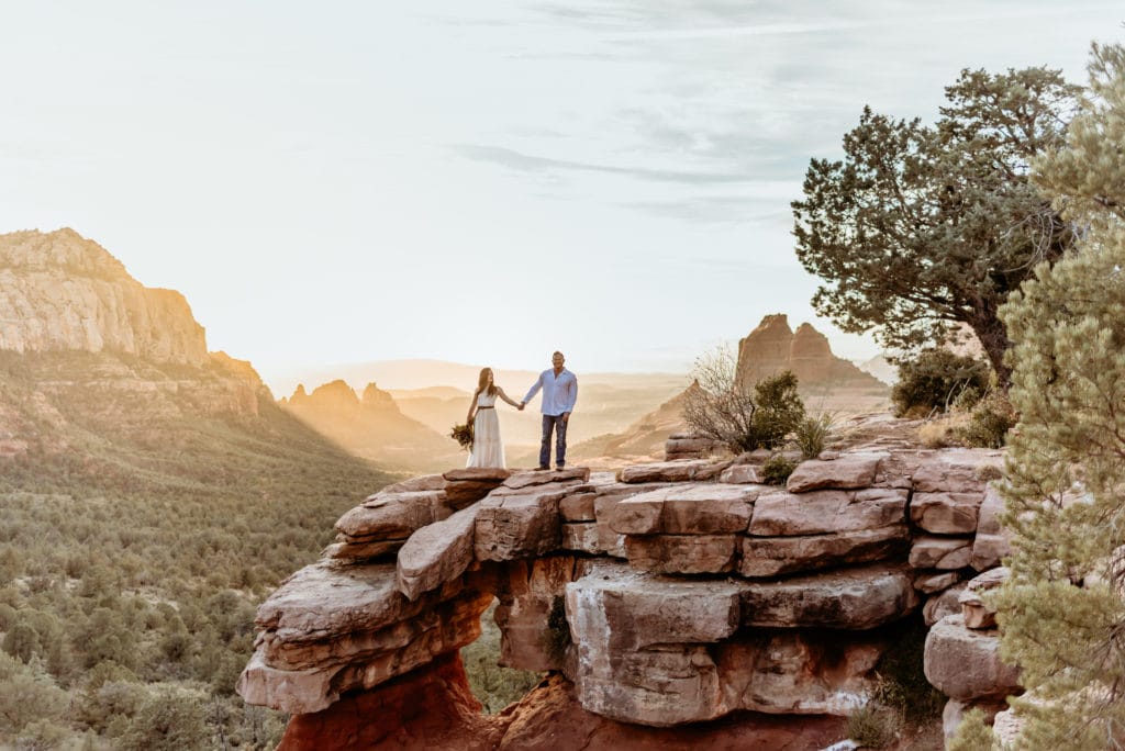 Elopement couple standing on Merry Go Round Rock as the sunset lights up the sky behind them