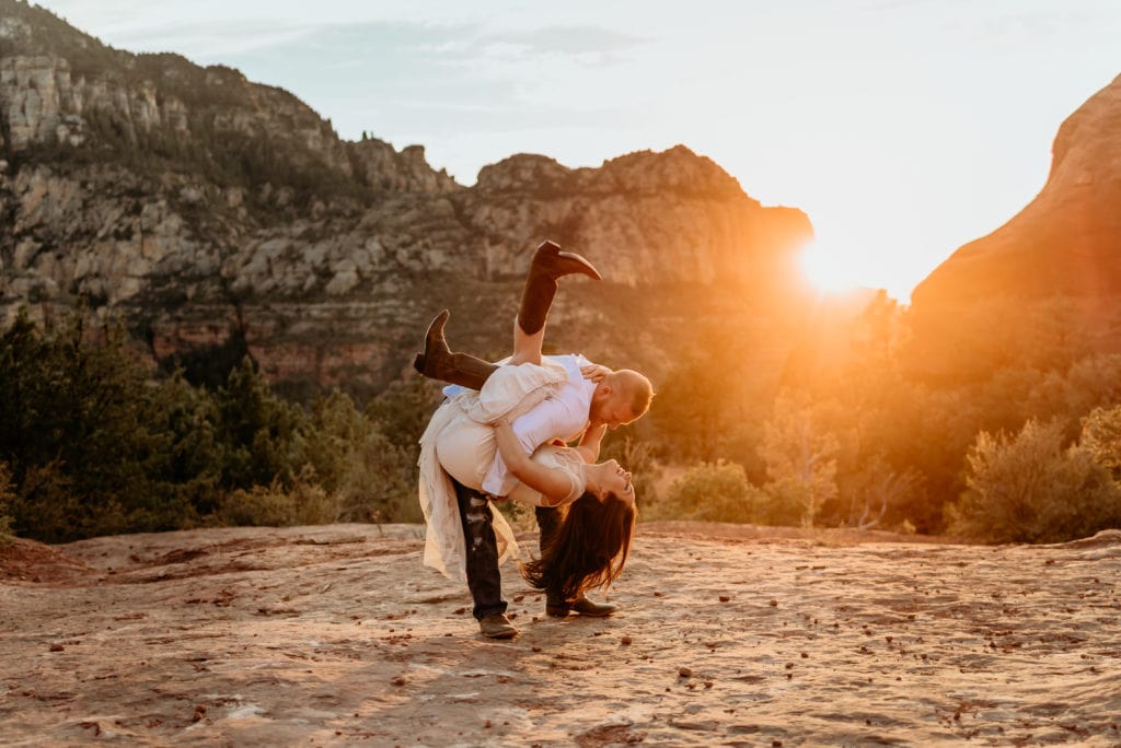 Groom dips bride as they dance on a large red rock