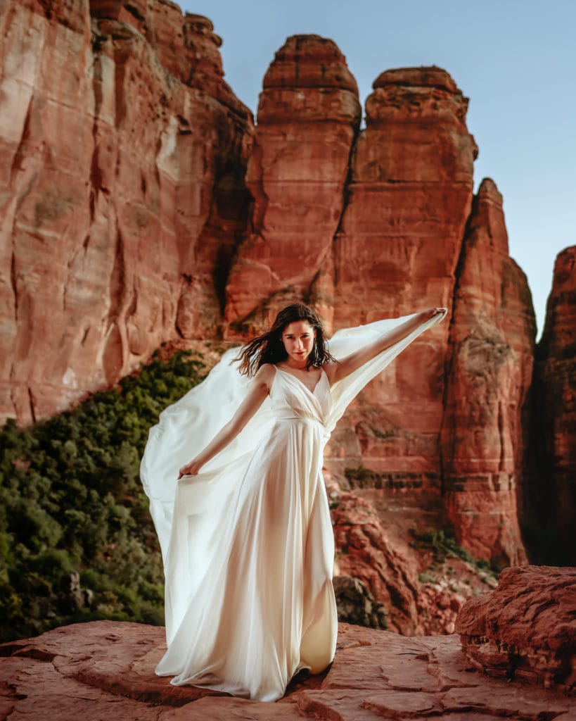 Bride holding flowing wedding dress as a cape on her Cathedral Rock elopement in Sedona, AZ