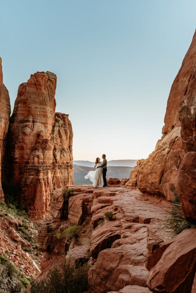 Sunset glow and blue skies enveloping elopement couple at the peak of Cathedral Rock in Sedona