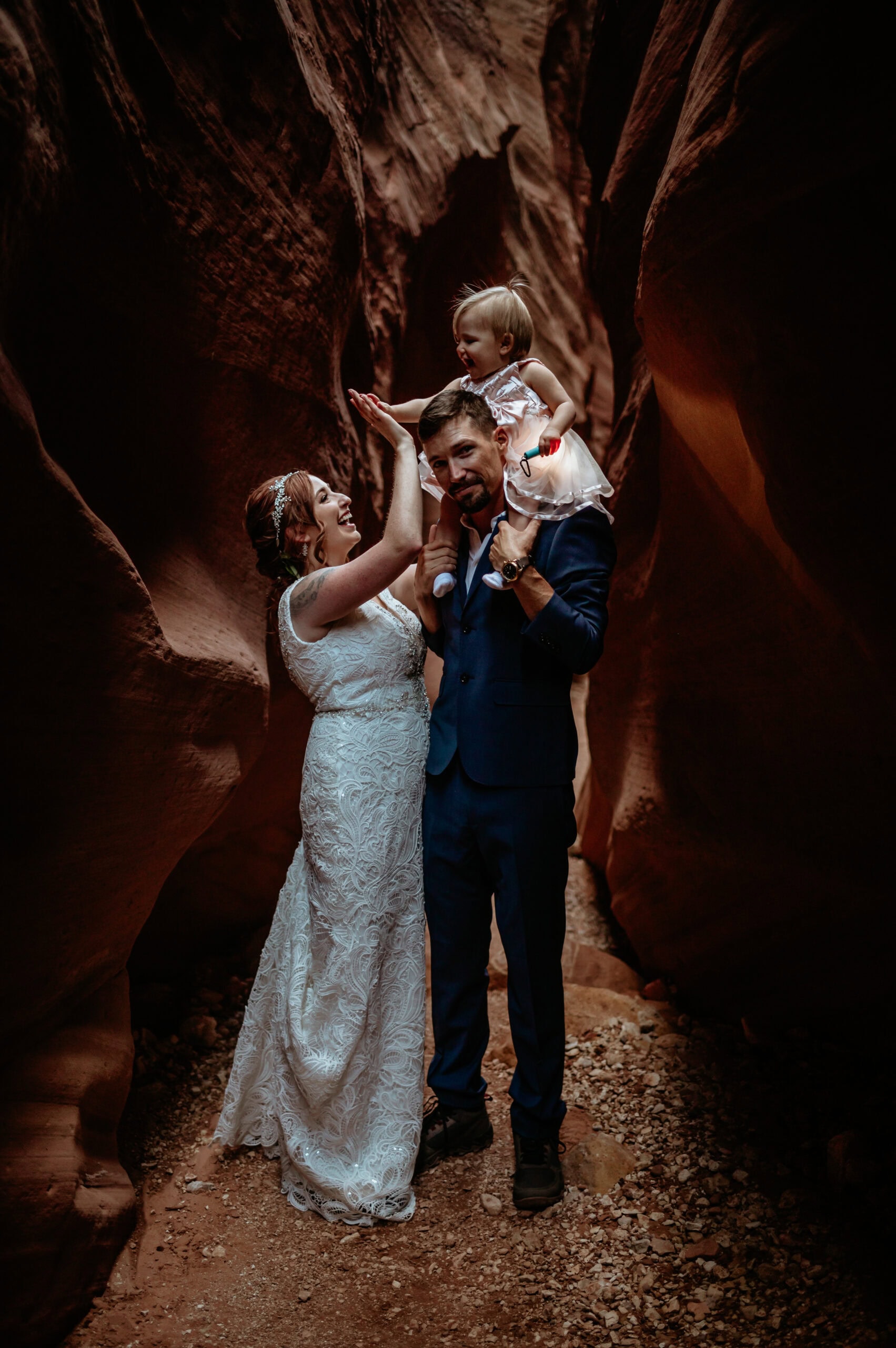 Mom and baby give a high five with baby girl on dad's shoulders inside slot canyon by Arizona elopement photographer Stratus Adventure Photography