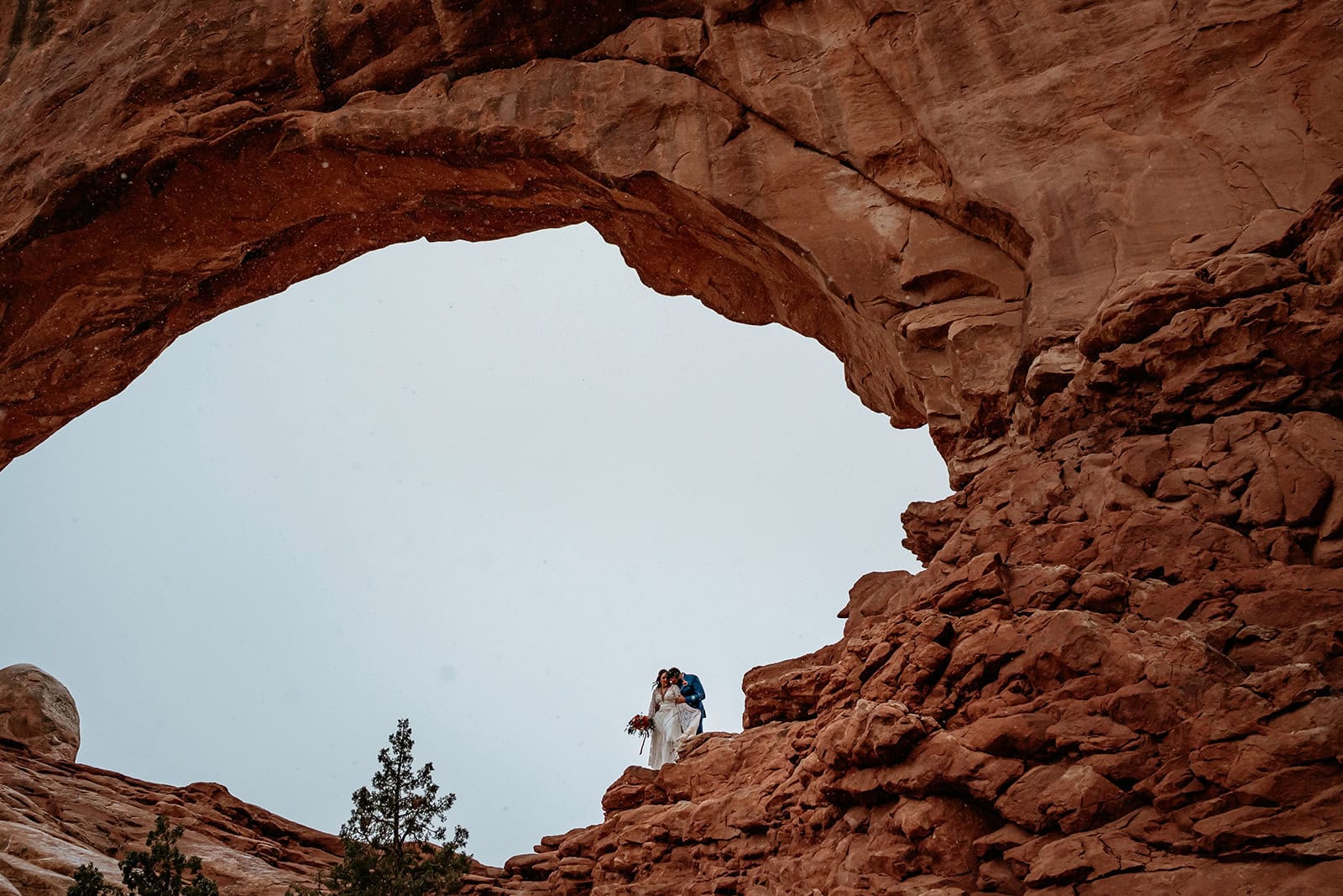 Elopement couple standing under a wintery arch by Moab Elopement photographer Stratus Adventure photography