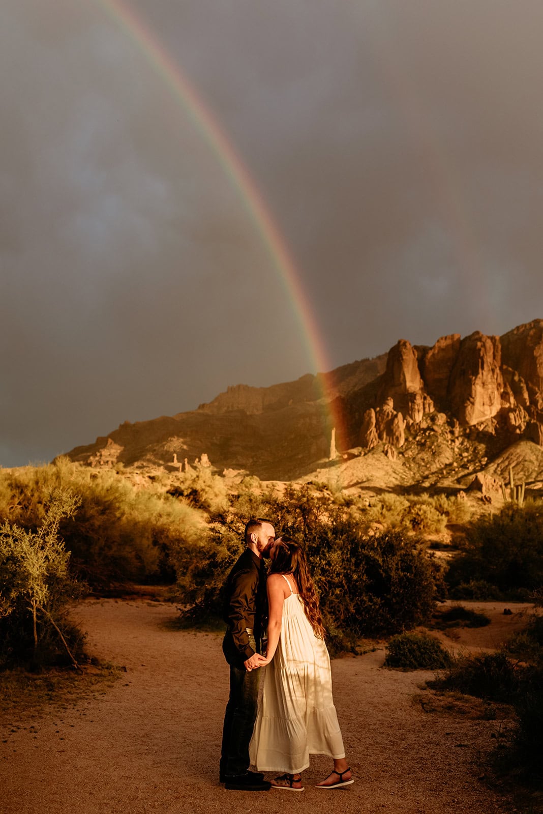 Couple going in for a kiss with a bold rainbow in the sky behind them during their Phoenix elopement, shot by Stratus Adventure Photography