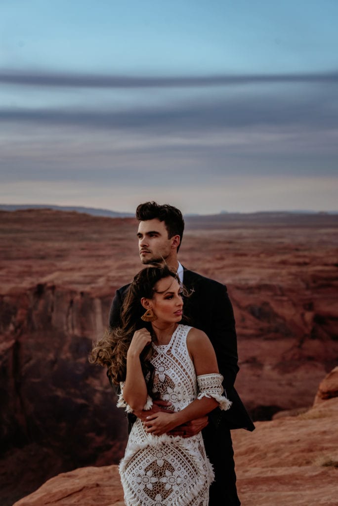Wind sweeps bride's hair as she and groom look into the distance during Page sunset elopement