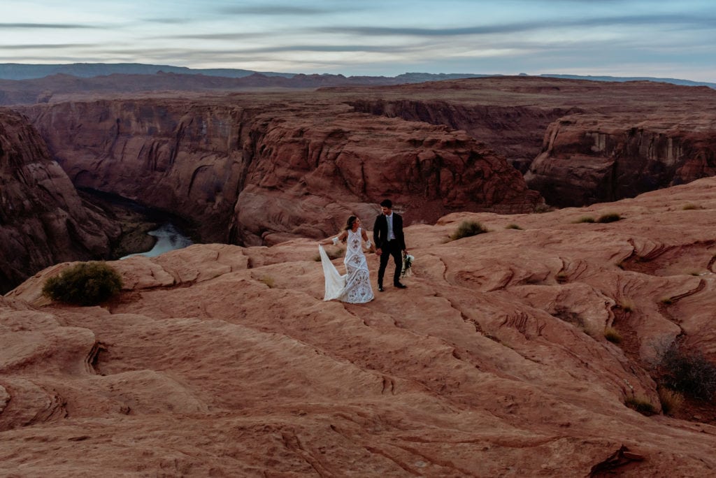Elopement couple walk hand in hand up the sandstone at Horseshoe Bend