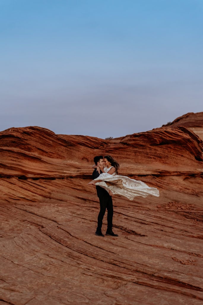 Groom swinging bride through the air as her Rue De Seine Lace Boho wedding dress flies behind her