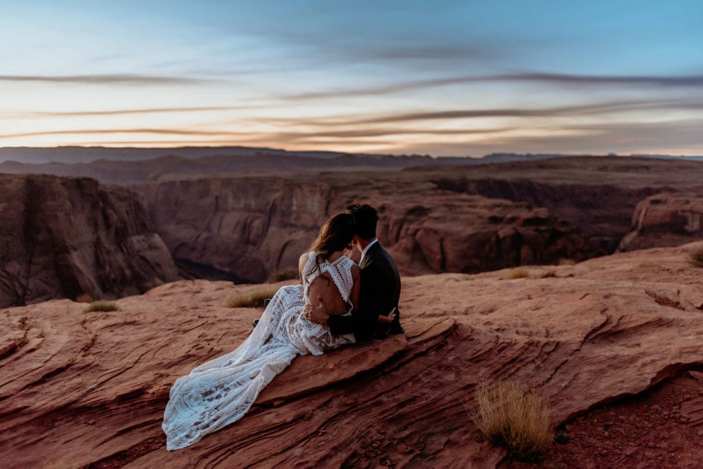 Couple relaxes during Horseshoe Bend elopement. Shows lacy back of bride's Rue De Seine boho wedding dress