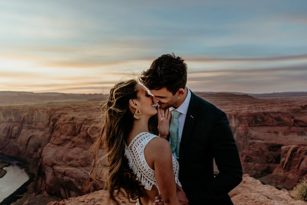 Couple on a windy ledge of Horseshoe Bend with the sunset behind them