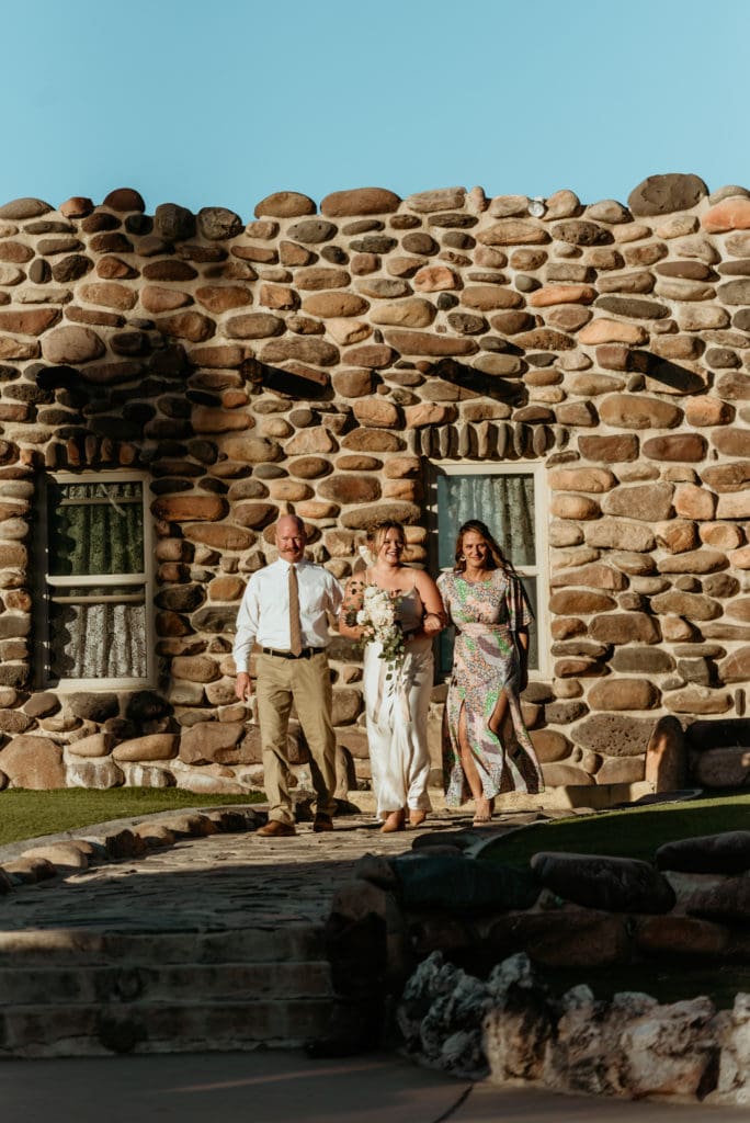 Bride surrounded by her mom and dad walking down the isle during her Wranglers Roost wedding
