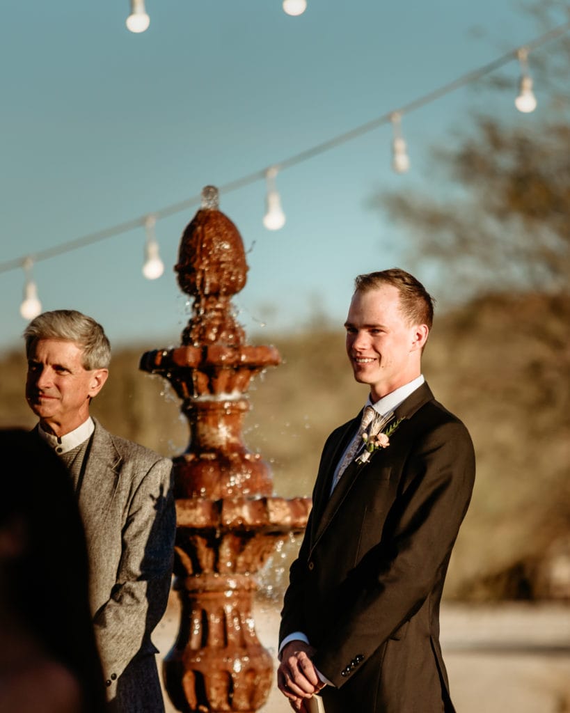Groom watching bride come down the walkway during their intimate wedding ceremony in the Arizona desert