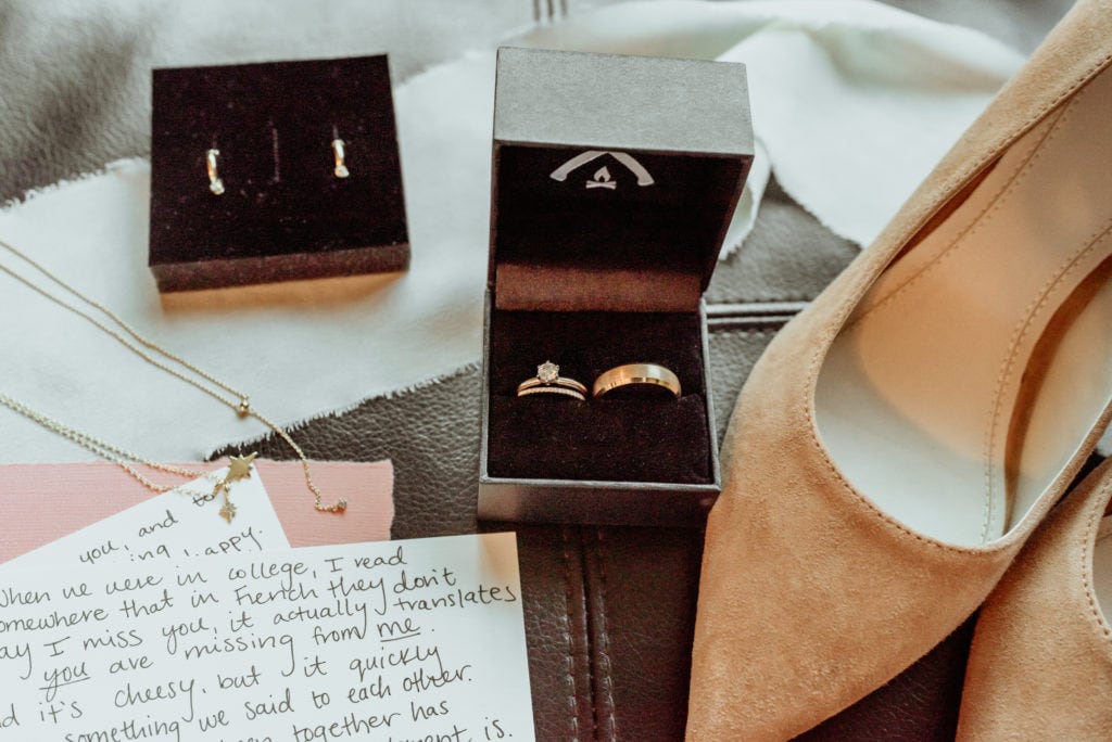 Detail shot with vows, rings, jewelry, and suede shoes