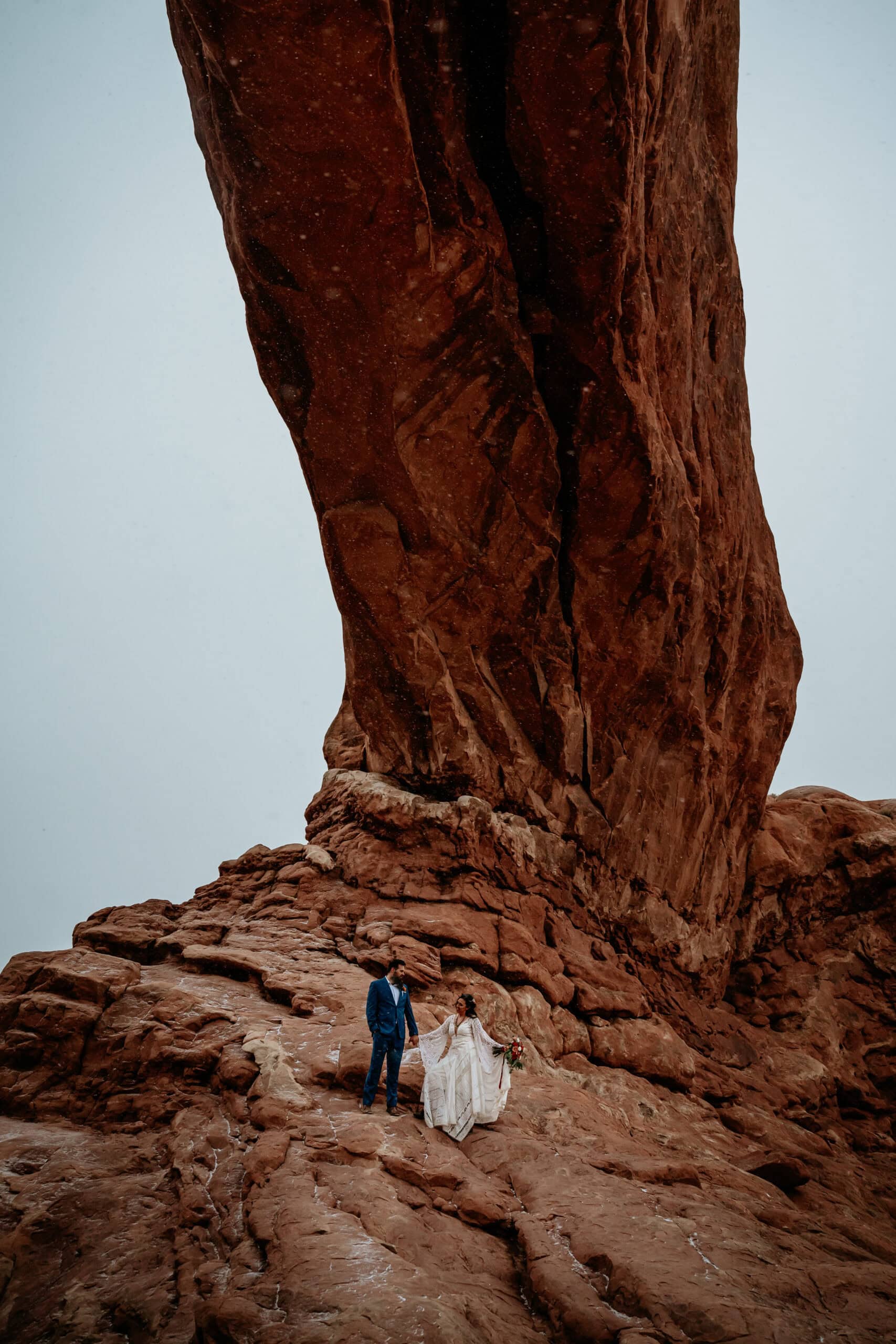 couple standing under a red rock arch by Moab Elopement photographer Stratus Adventure photography