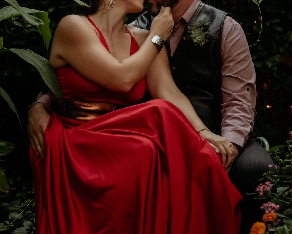 Bride draws grooms chin in for a kiss wearing her vibrant red sating wedding dress with copper belt