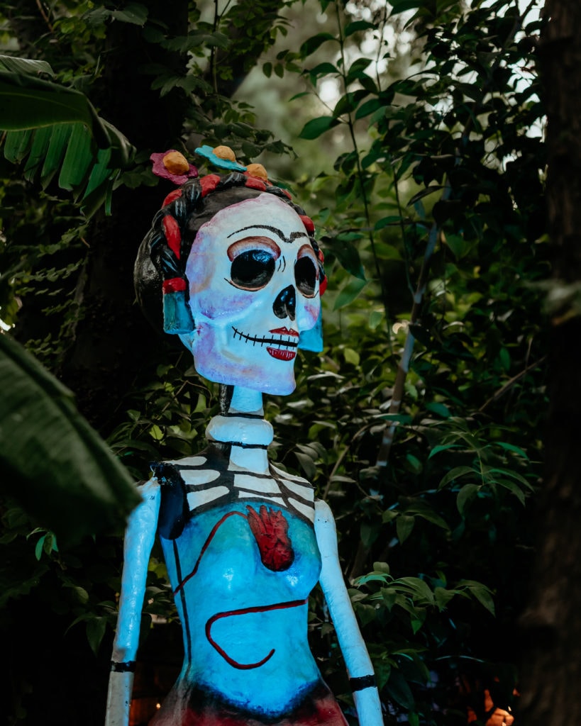 Intricate blue, red and white Dia De Los Muertos sculpture surrounded by jungle vines at the Tucson Desert Botanical Gardens