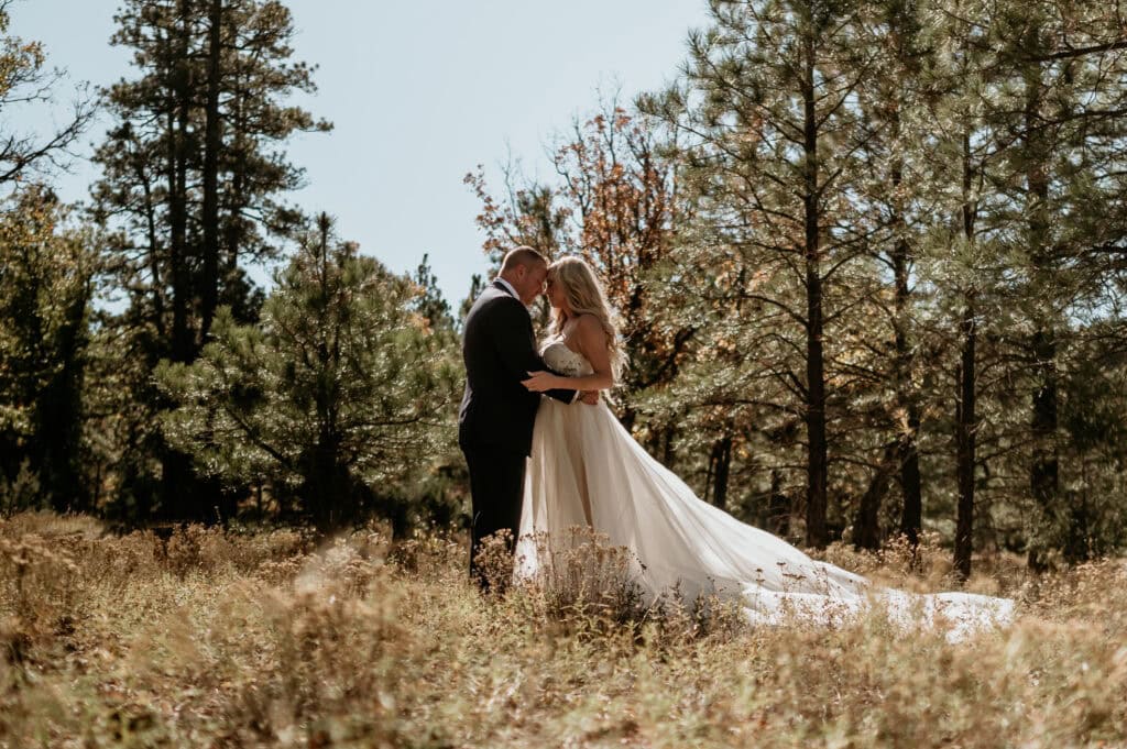 couple embraces in an open field surrounded by pine trees during their Flagstaff Arizona elopement