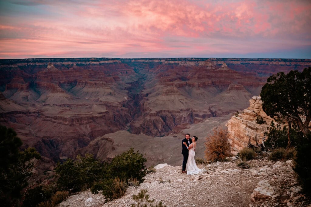 Couple watching the vibrant pink and purple sunset while standing on the Grand Canyon rim during Arizona elopement captured by Stratus Adventure Photography