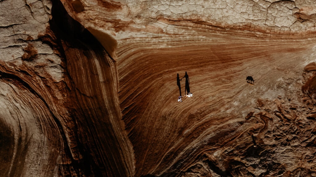 Shadows of bride and groom dancing while their dog walks towards them from above during their elopement in Arizona